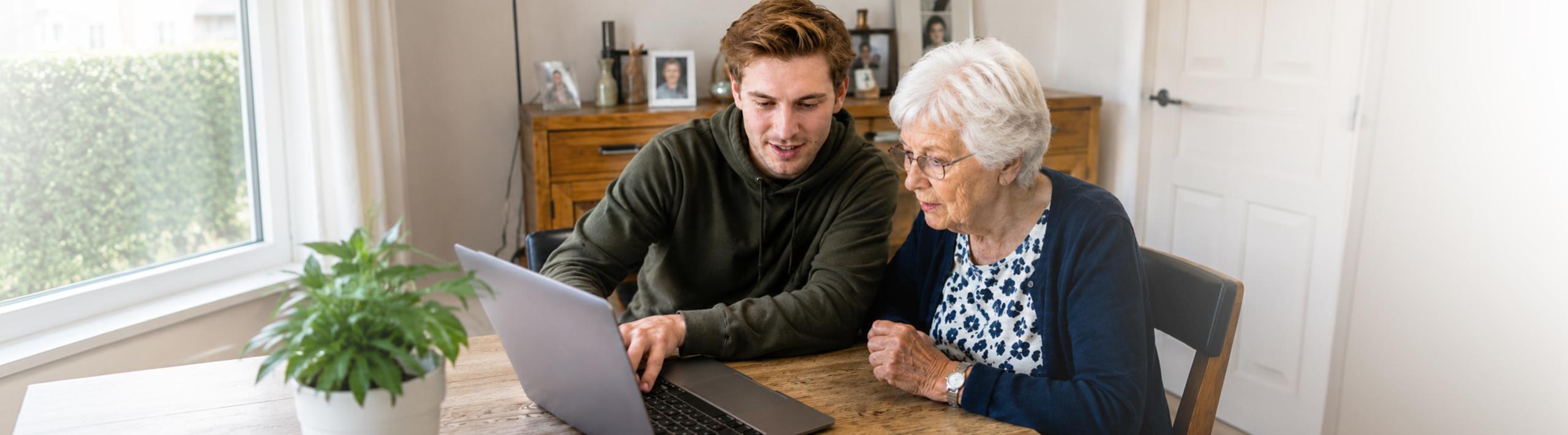 Jongeman geeft uitleg op de computer aan een oudere vrouw.